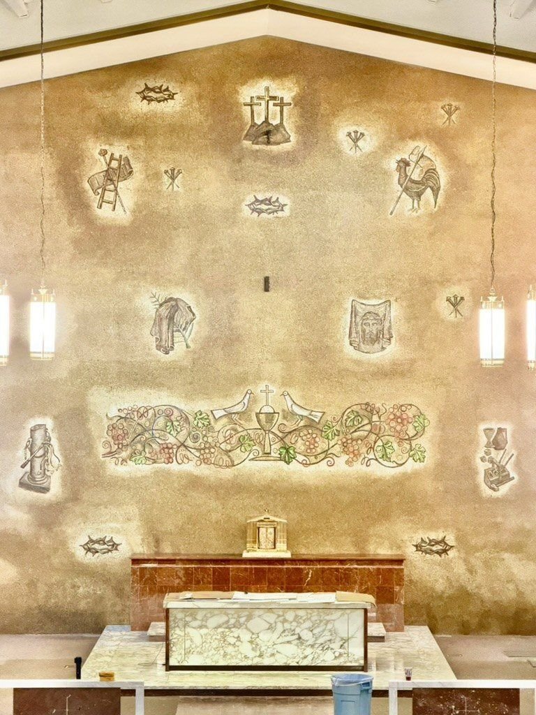 Restored mosaic wall with religious symbols and a grape-and-chalice band above the altar.