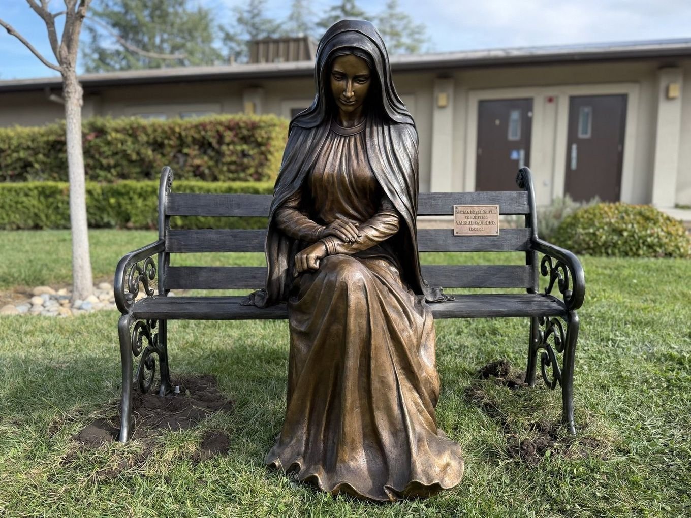 Full view of the bronze statue of Mary seated at one end of a bench with an open seat beside her.