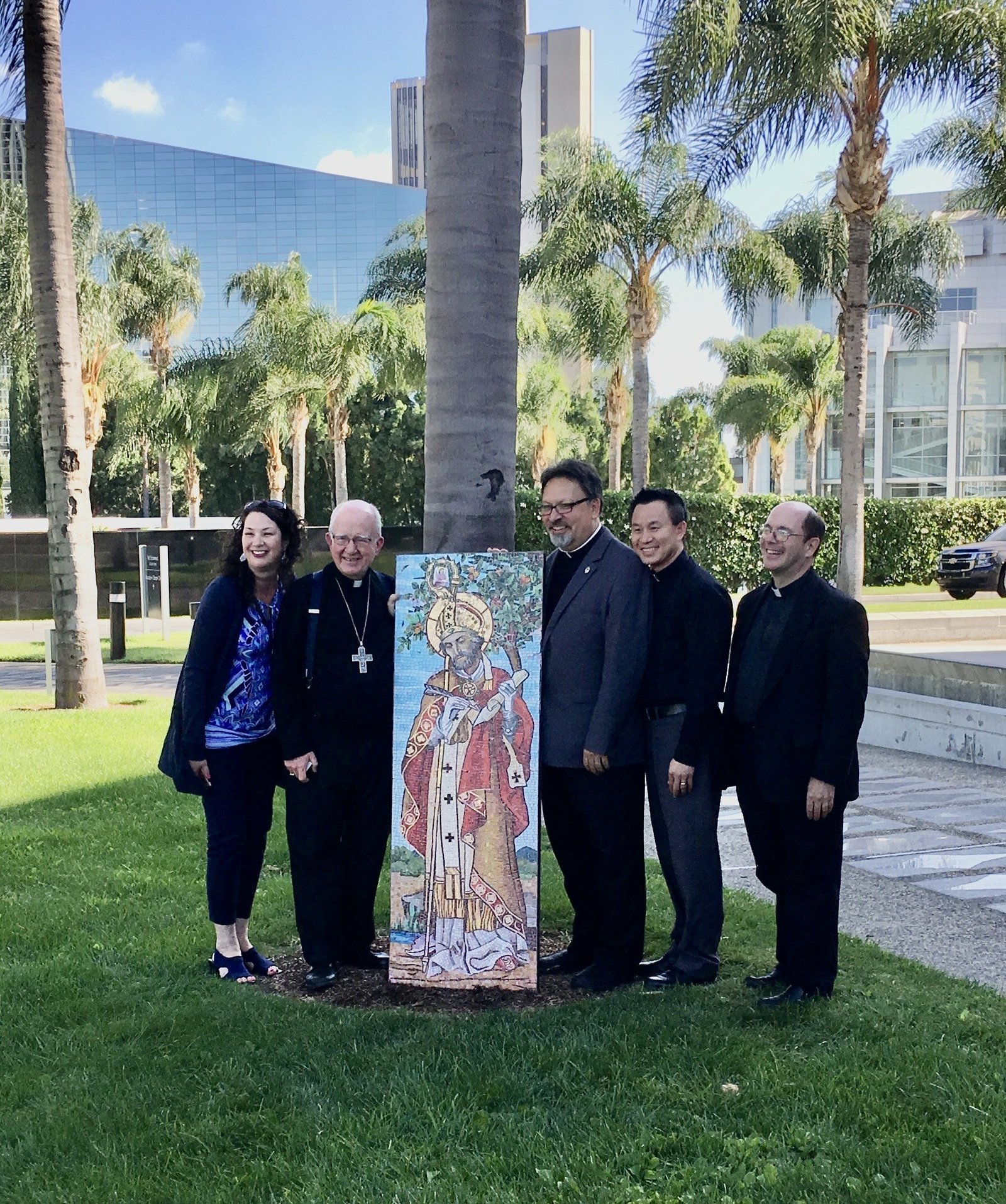 A group standing beside a tall mosaic of a robed, mitred figure on the cathedral campus