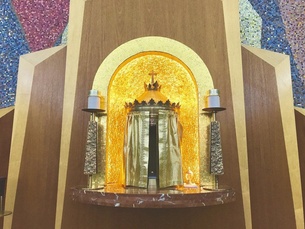 Illuminated gold mosaic niche surrounding the tabernacle above the marble platform.