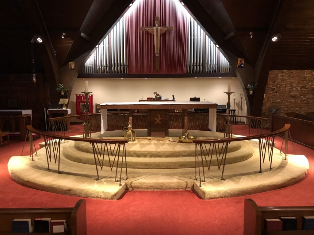 Raised curved chancel with red carpet, angular rail supports and a crucifix above the altar