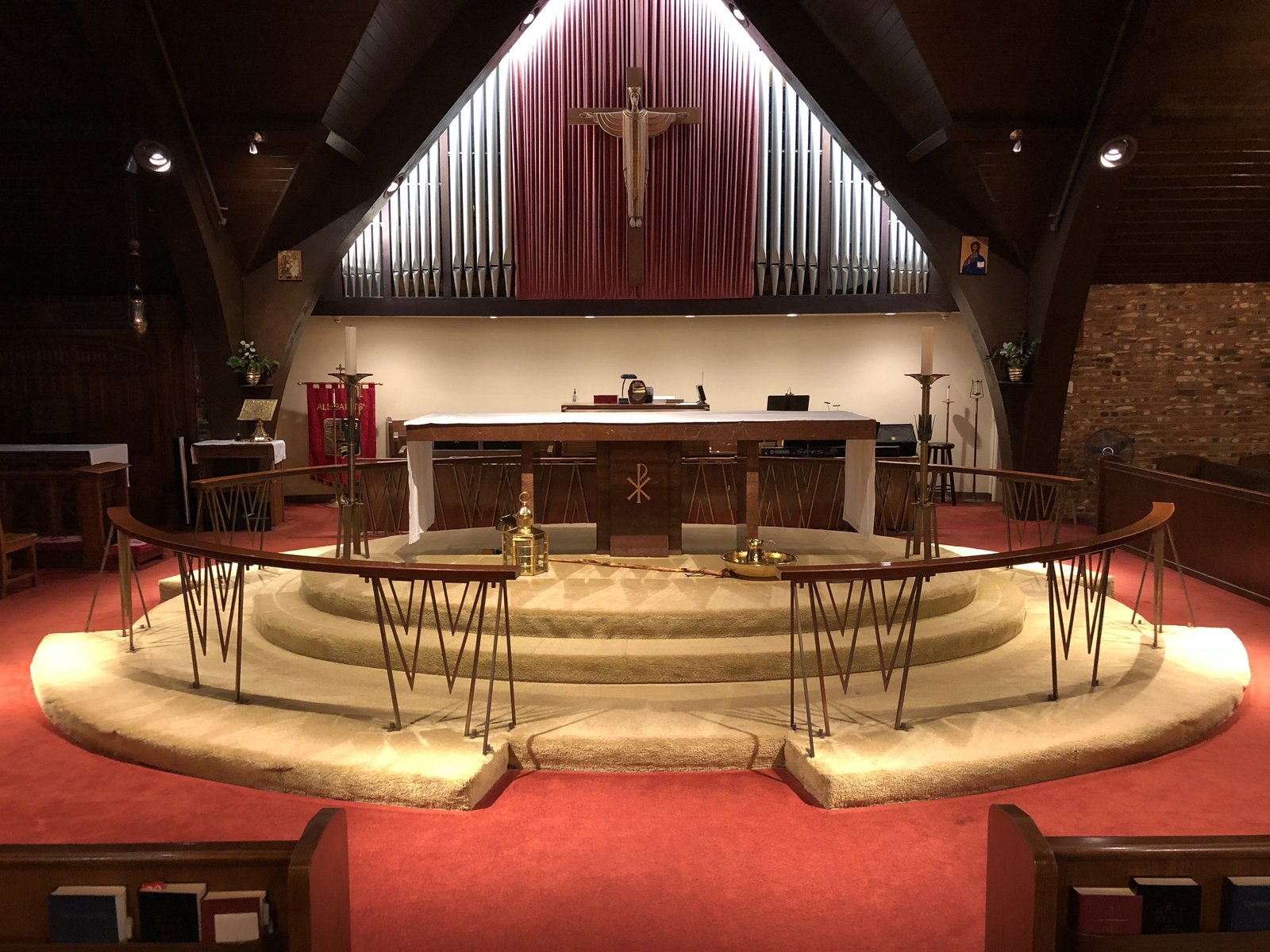 Raised curved chancel with red carpet, angular rail supports and a crucifix above the altar