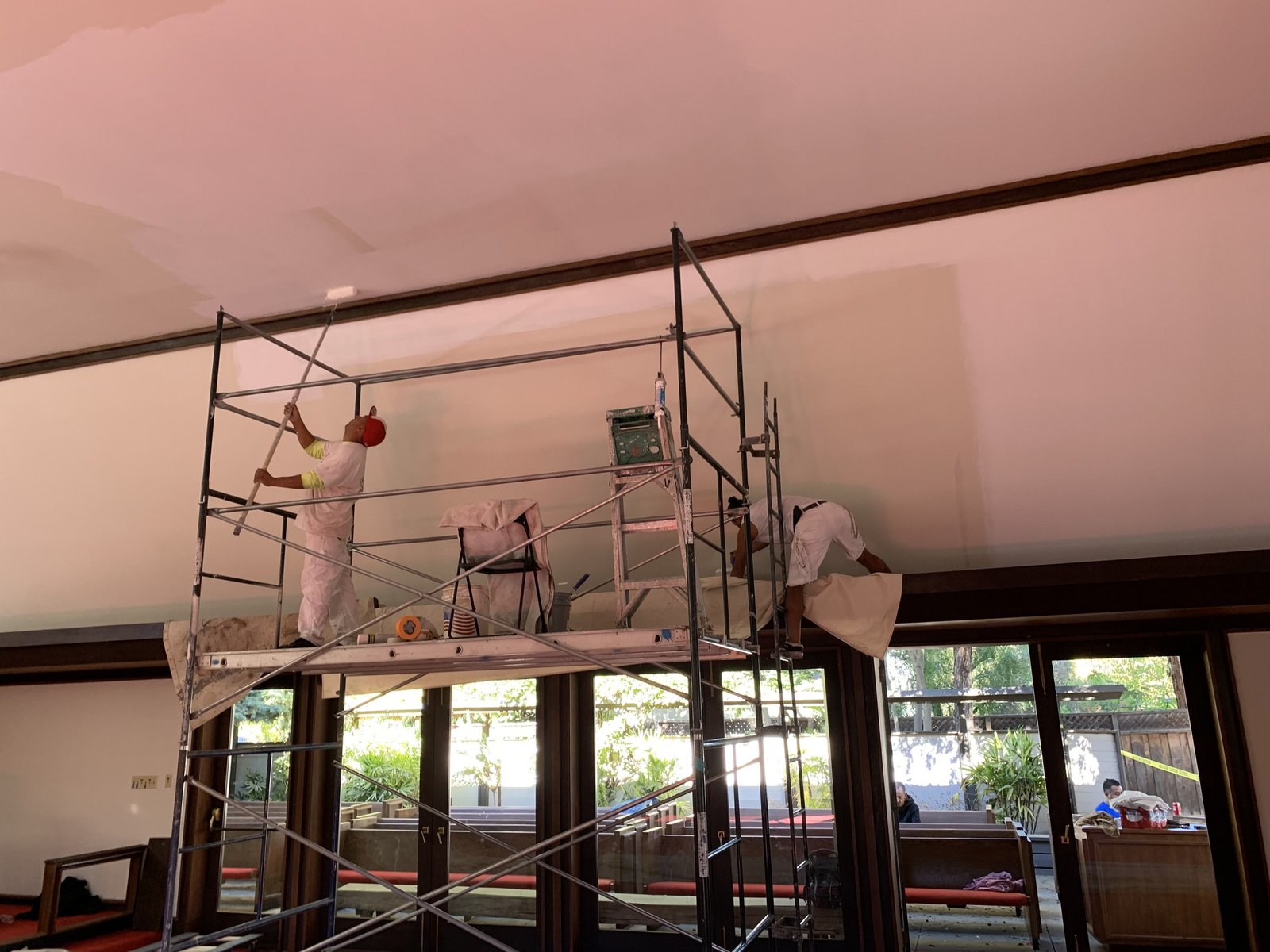 Workers on scaffolding painting the high white ceiling beside dark wood trim