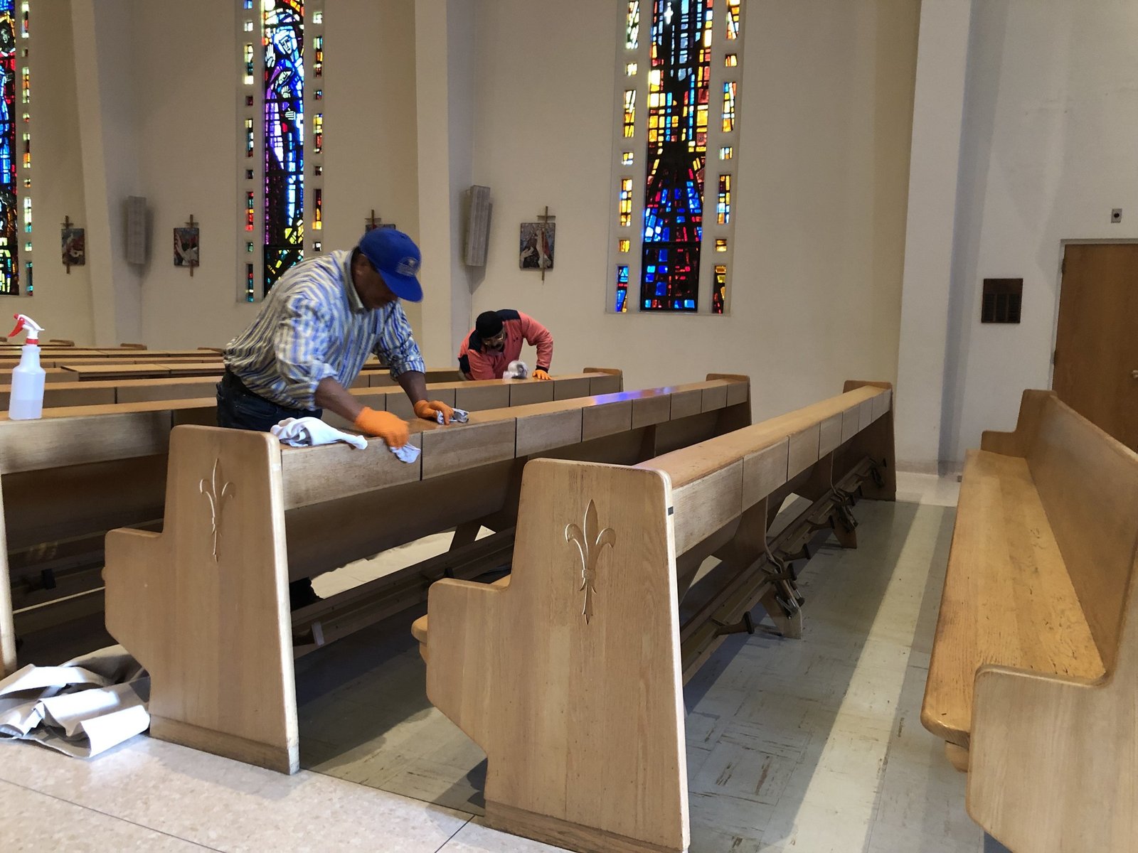 Workers wiping wooden pew backs with cloths beneath stained glass windows