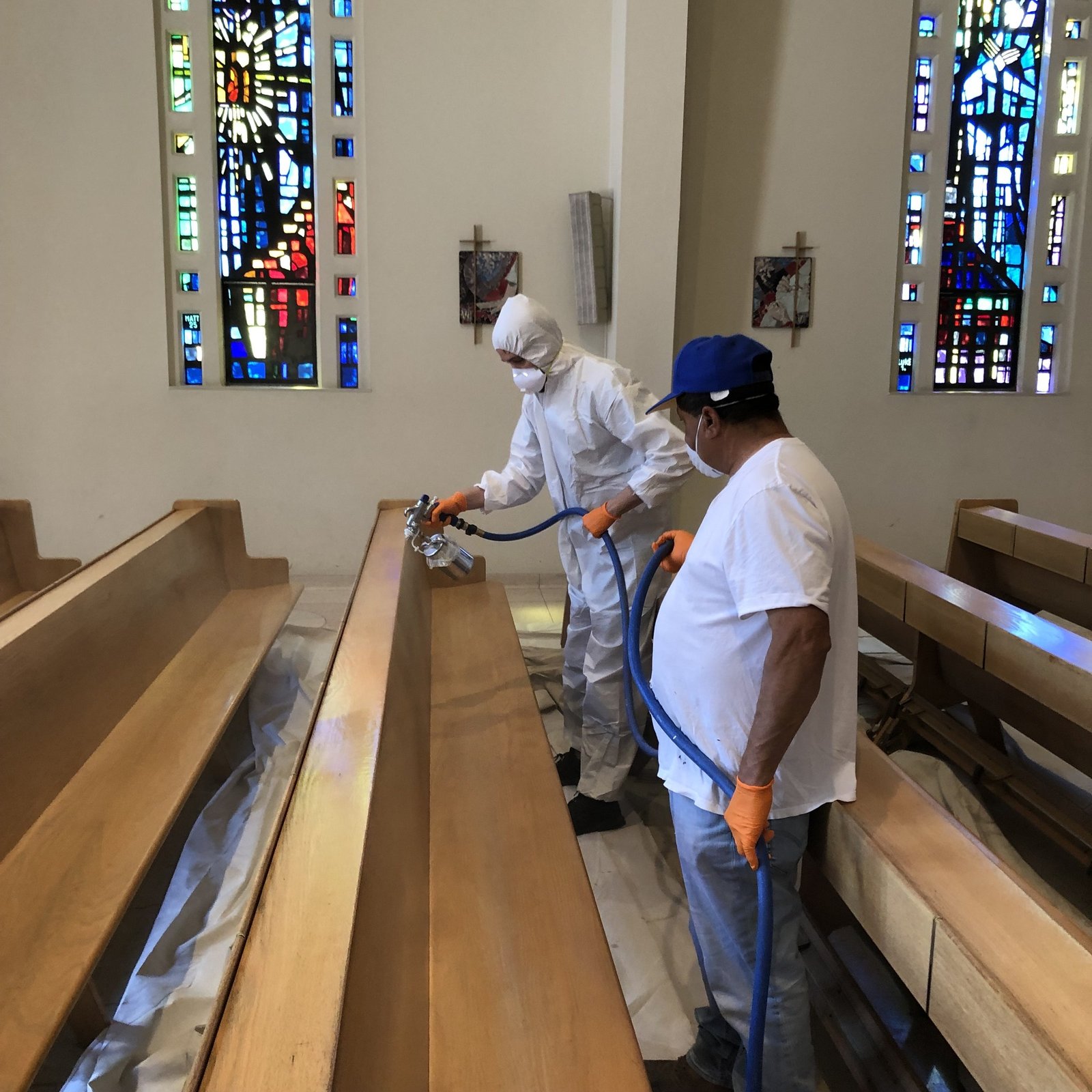 Workers applying a coating to a wooden pew with a spray gun