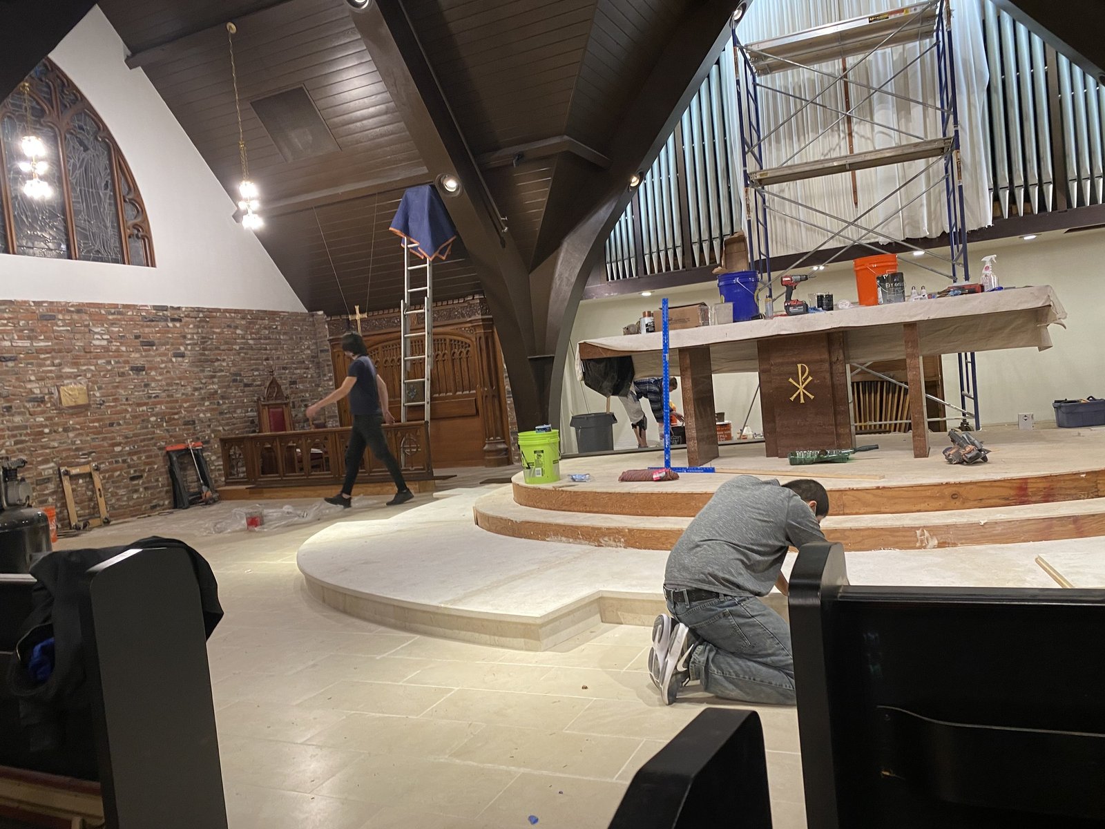 Worker kneeling near the curved chancel steps with tools and scaffolding around the altar