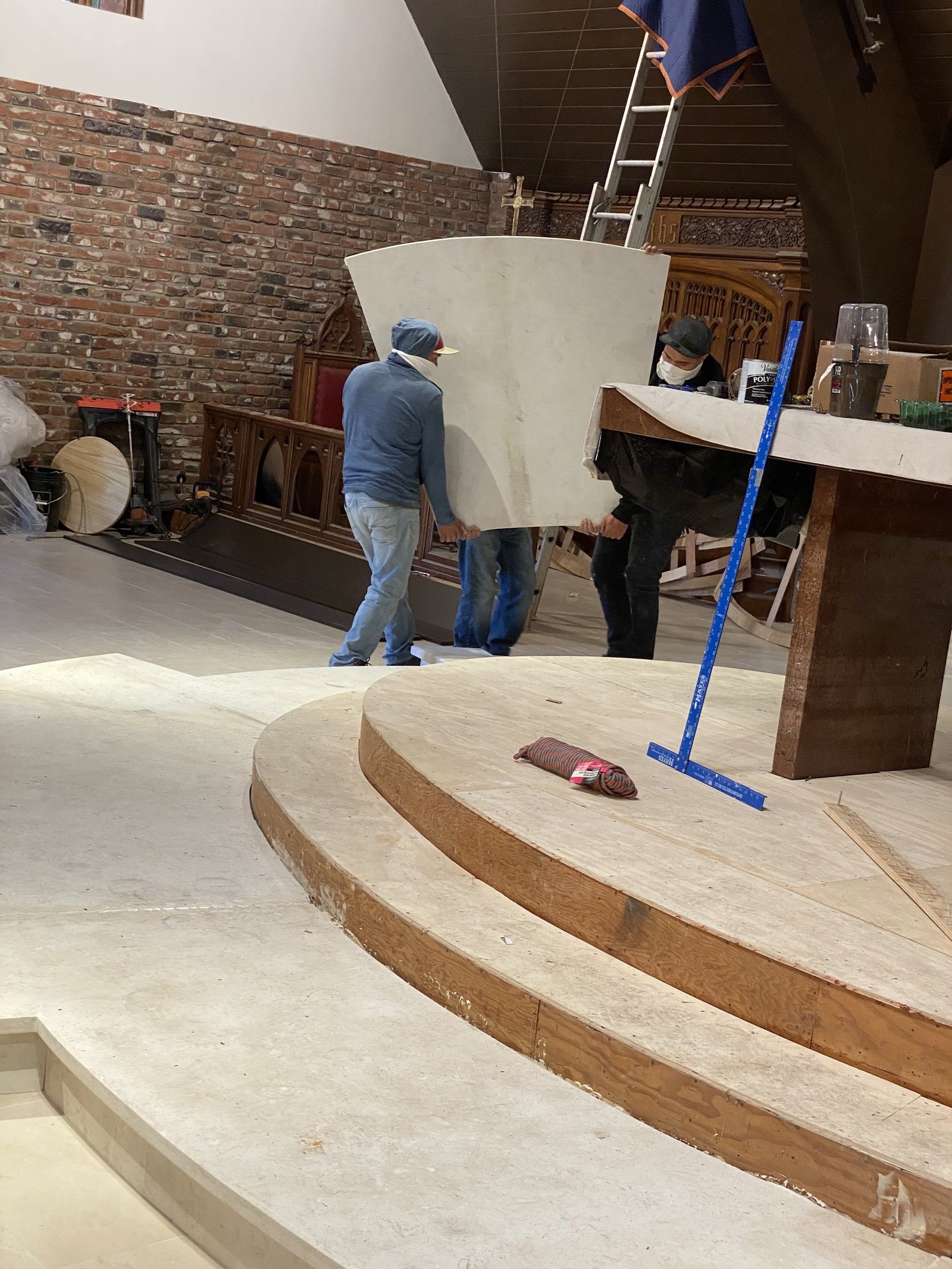 Workers carrying a large curved pale panel beside the raised chancel