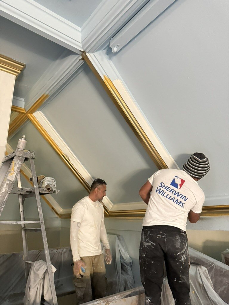 Two craftspeople working on the decorative ceiling trim.