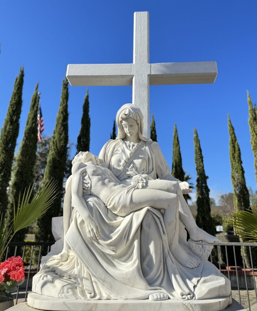 Restored outdoor Pietà on its pedestal beneath a tall cross.