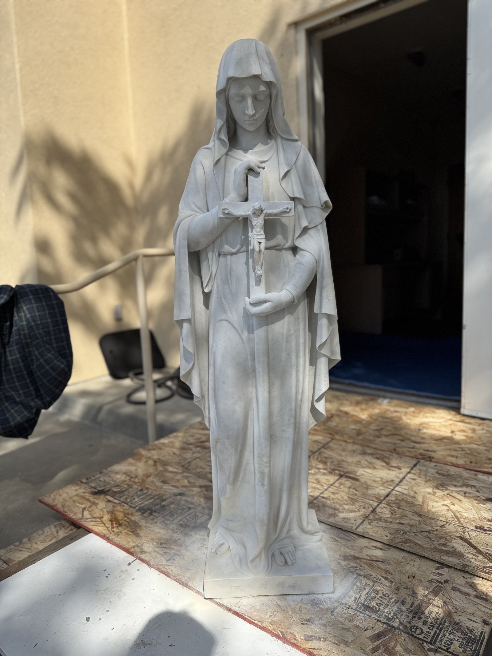 Restored statue of Mary holding a light-colored crucifix, shown full length.