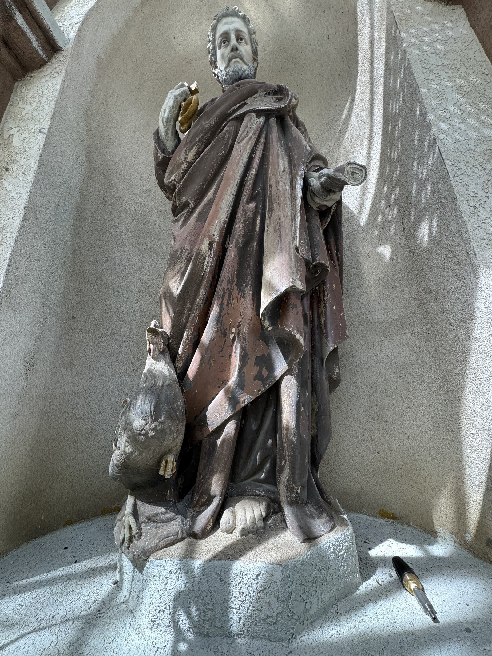 Weathered terracotta statue holding a scroll with a bird at its feet.