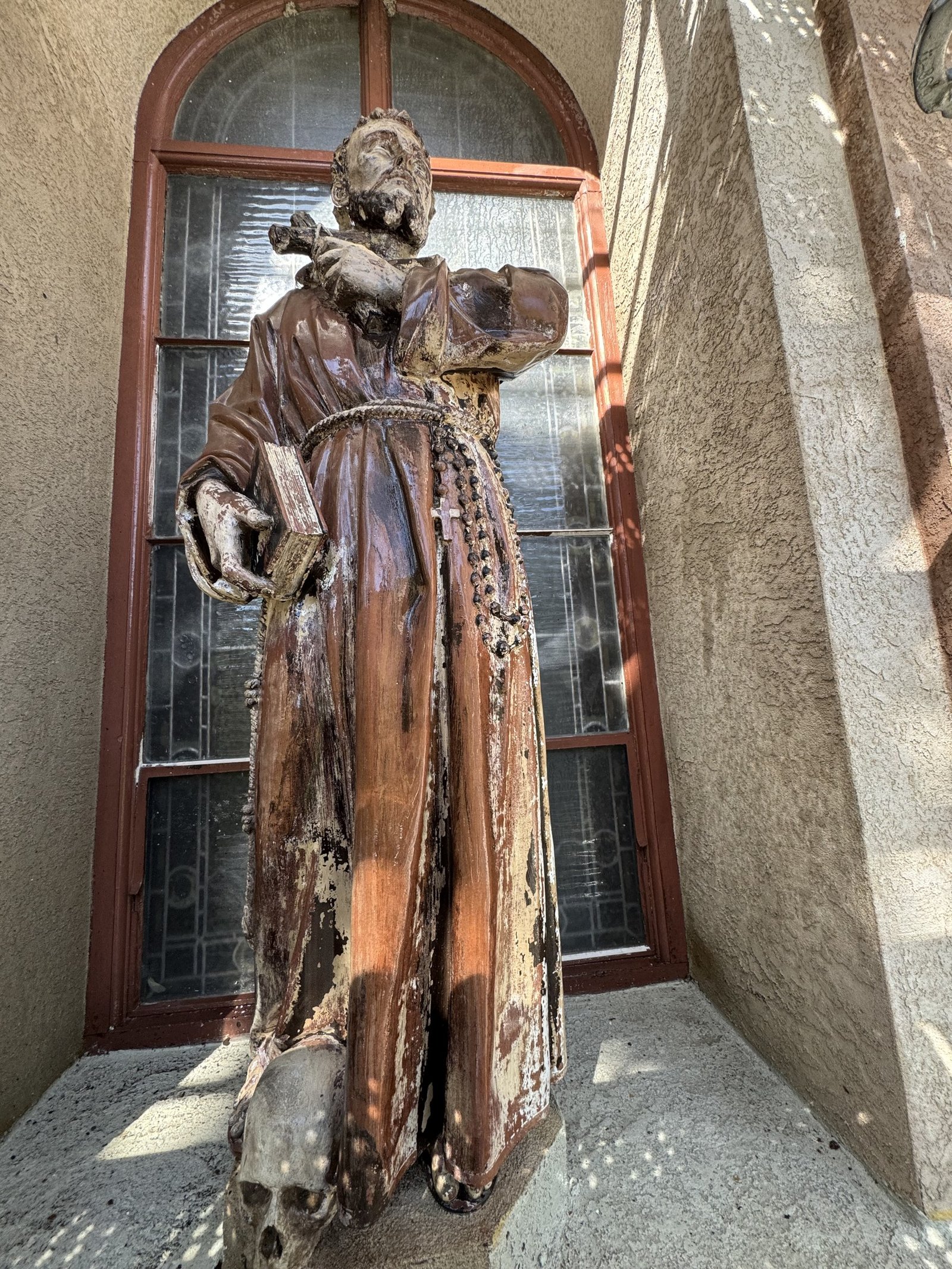 Terracotta statue with a weathered finish in front of an arched church window.