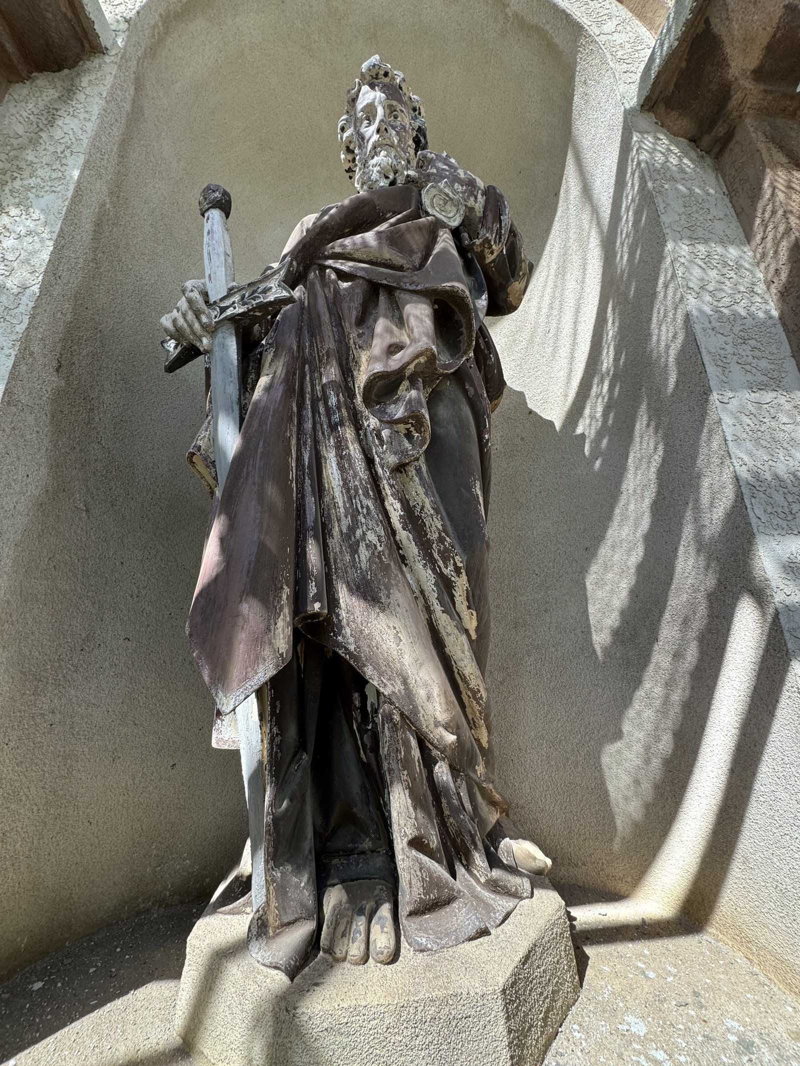 Sword-bearing terracotta statue with a weathered finish in an exterior niche.