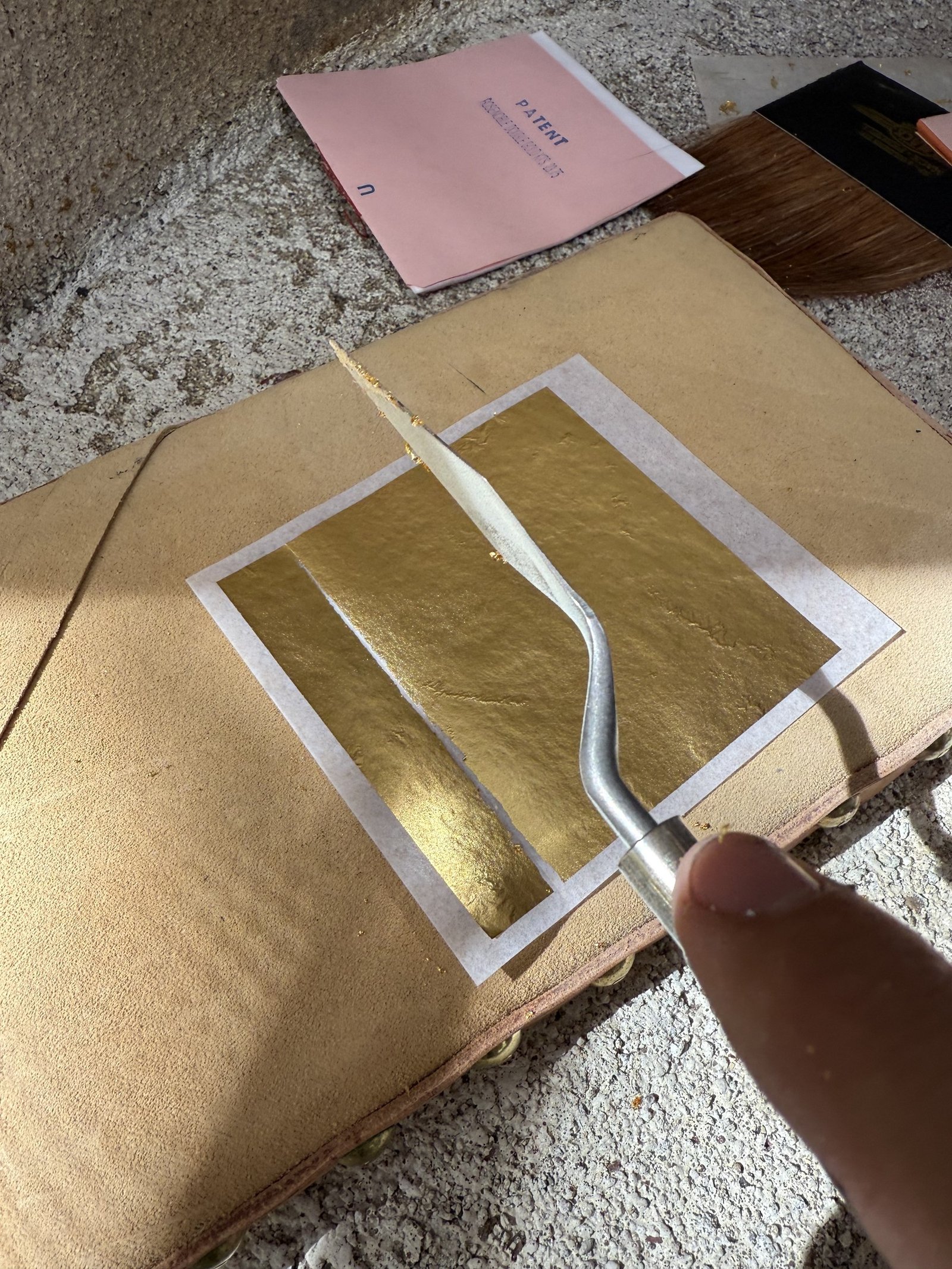 Sheet of gold leaf and a knife on a work surface.