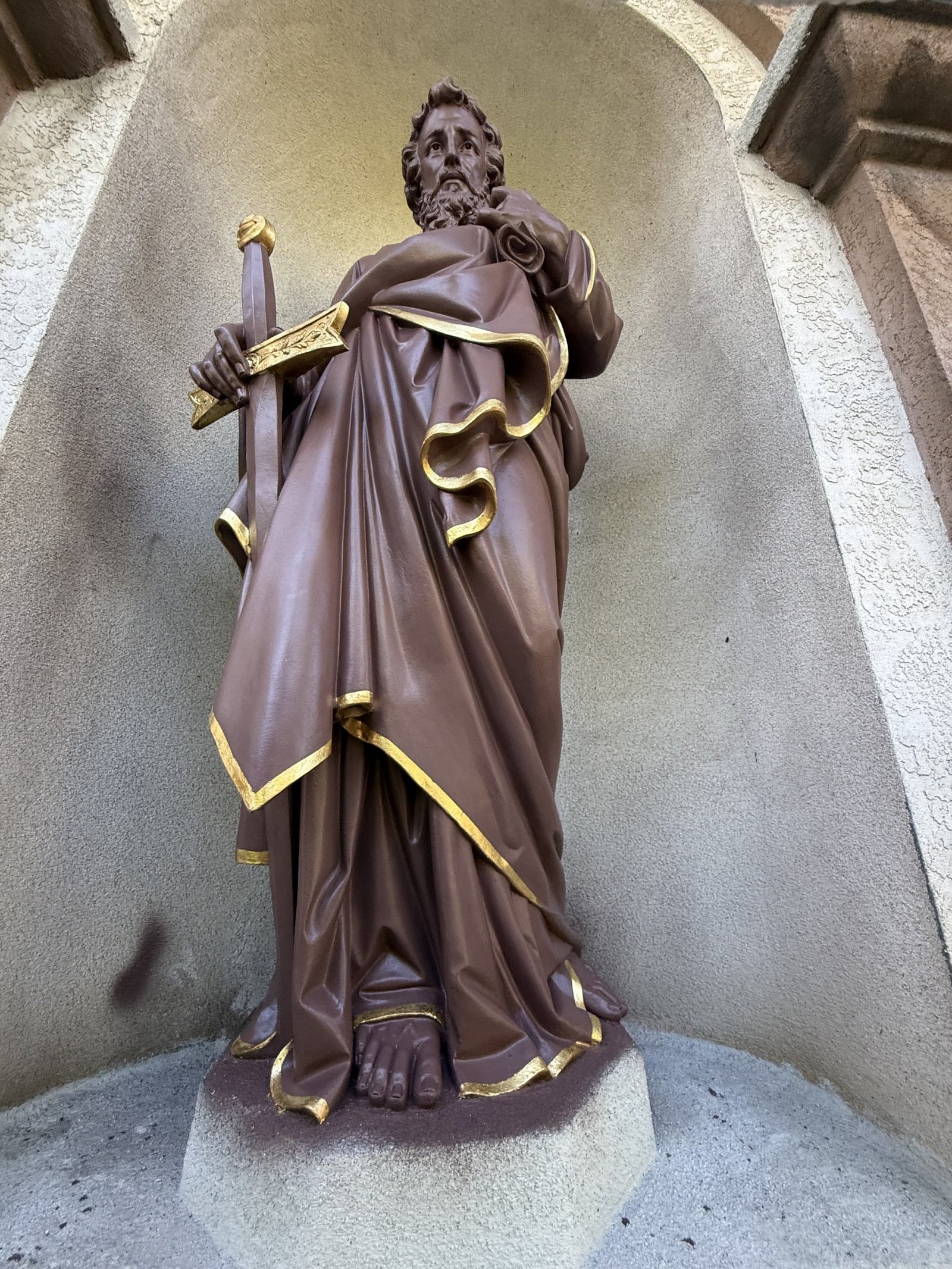Restored terracotta statue with a sword and gilded robe edges in an exterior niche.