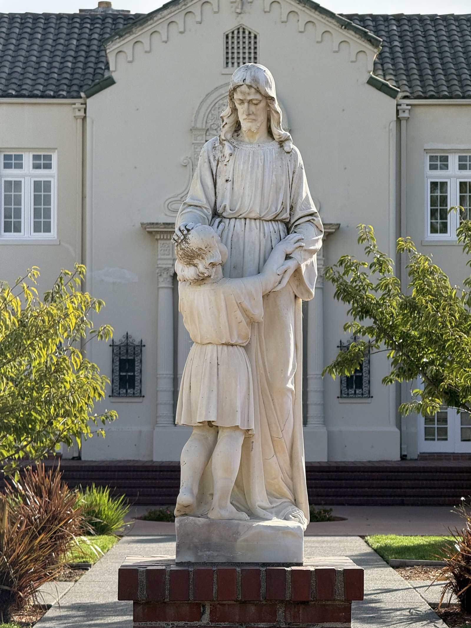 Standing figure and child on a brick pedestal in front of the church building.