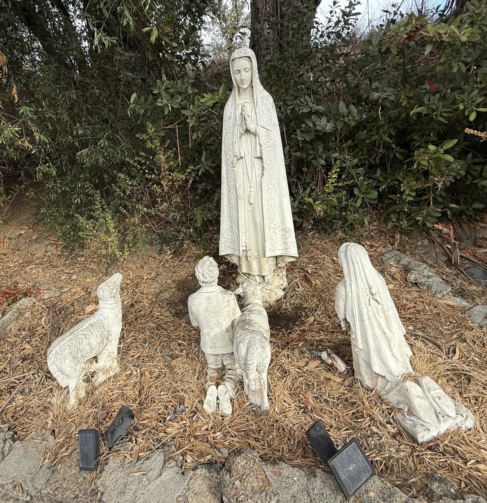 Weathered garden group with a veiled figure, kneeling children and sheep.