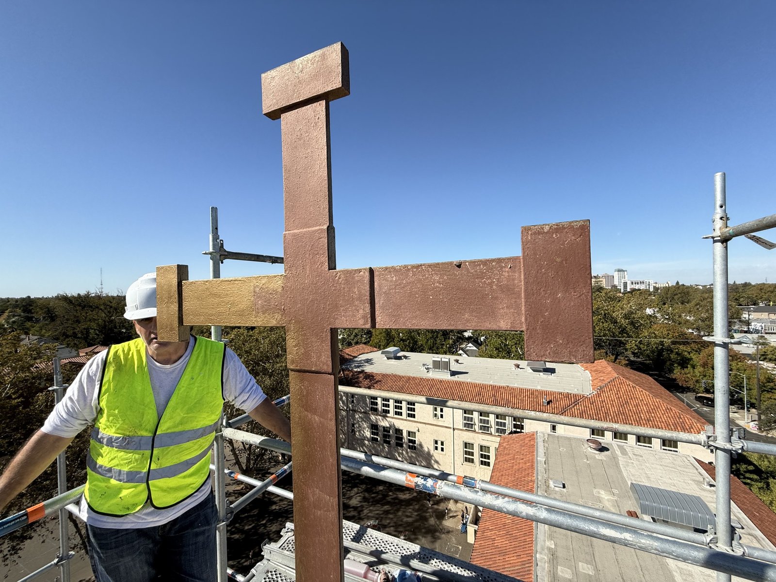 Rooftop cross with a brown surface and a gold-colored area on its left arm beside a worker