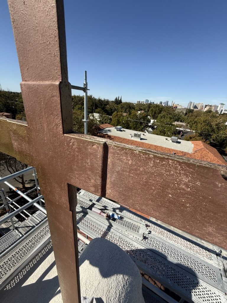 Close view of a rooftop cross with a rough brown surface and worn edges above scaffolding