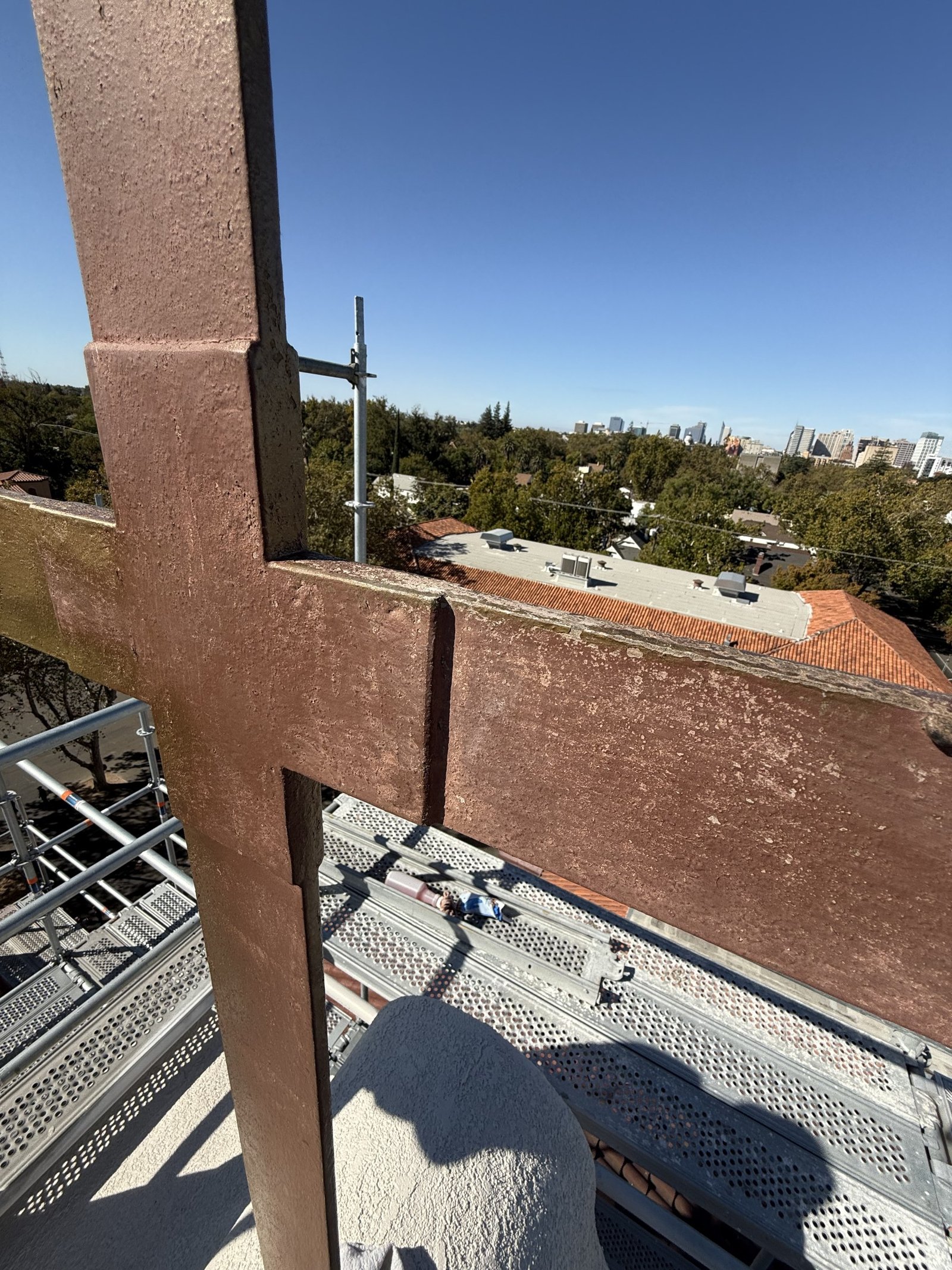 Close view of a rooftop cross with a rough brown surface and worn edges above scaffolding
