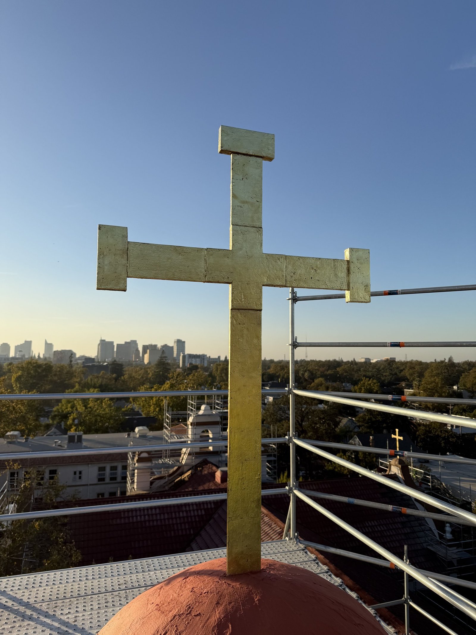 Gilded cross rising above a rounded roof feature with the Sacramento skyline beyond