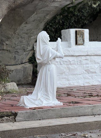 Restored kneeling marble figure with raised hands beside the stone grotto altar.