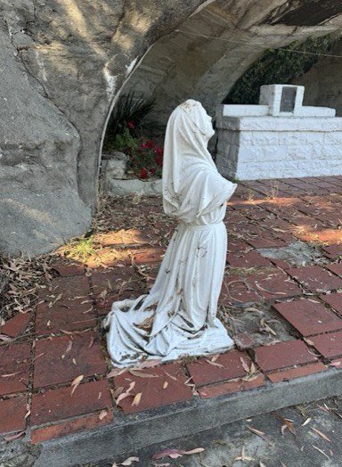 Kneeling hooded marble figure on a brick surface beside the stone grotto altar before restoration.