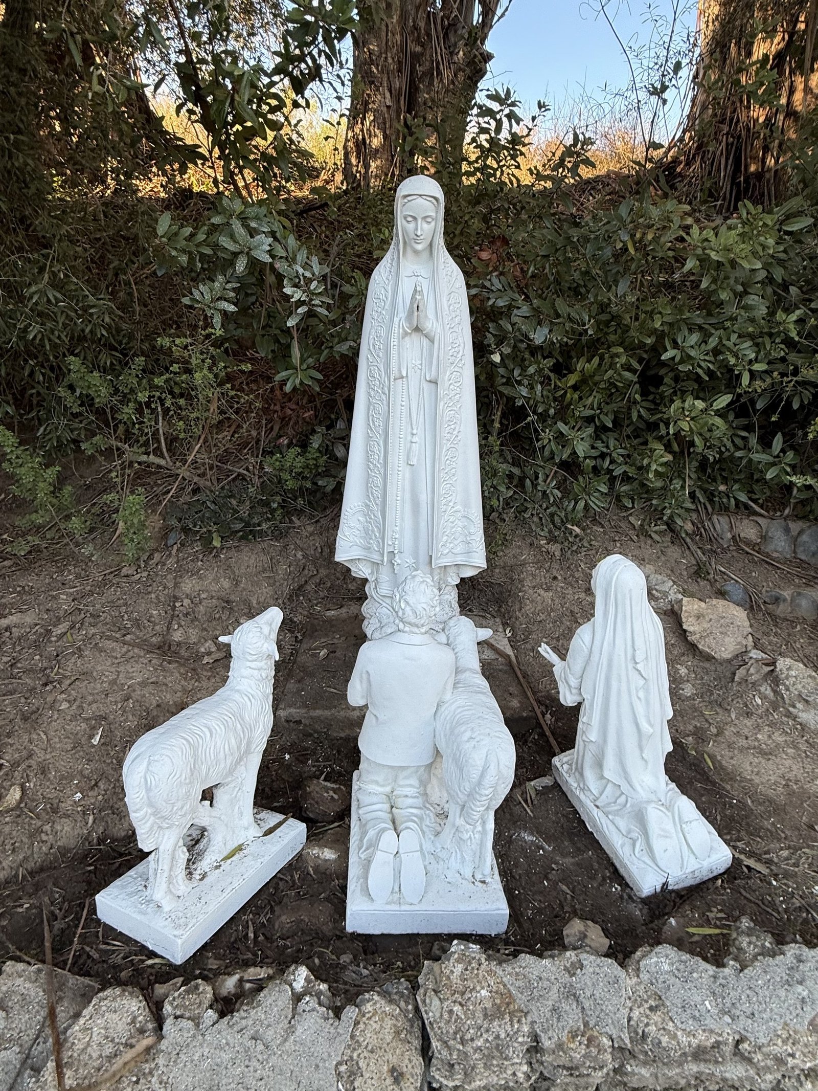 Restored veiled figure with clasped hands above kneeling children and sheep in the garden.