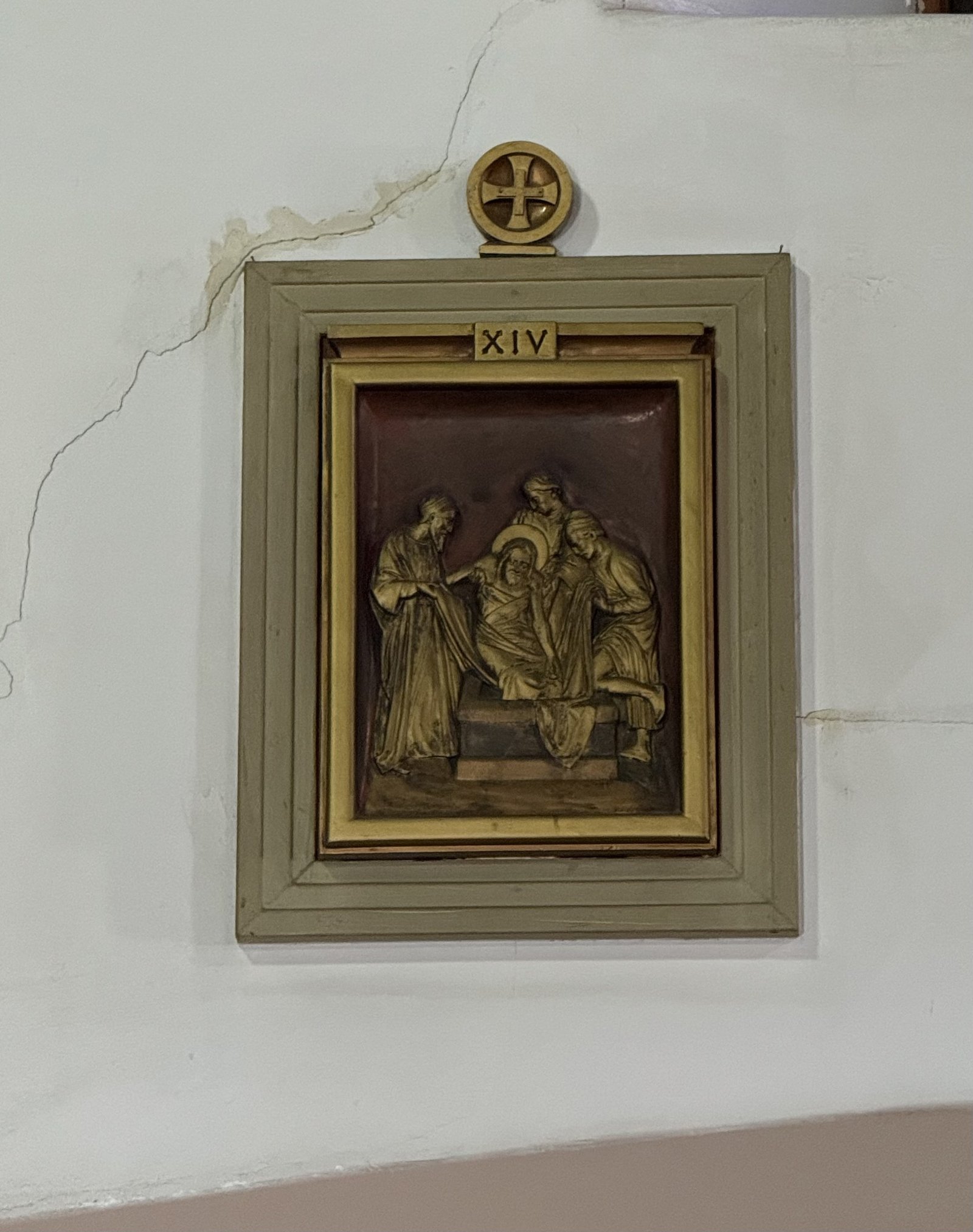 Station XIV relief with a pale frame and visible cracks in the surrounding wall.