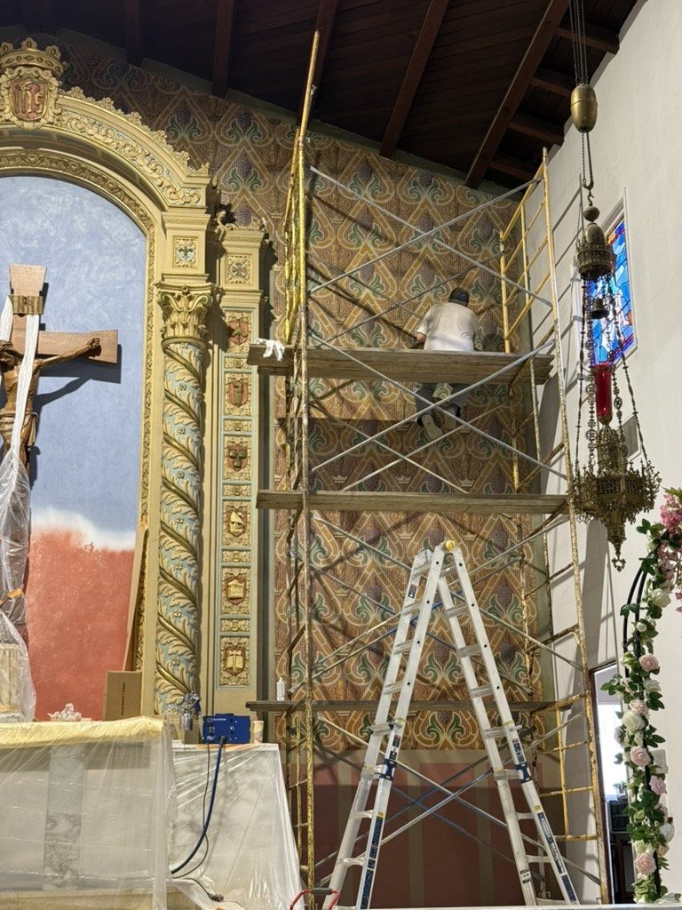 Worker on scaffolding beside the patterned wall and partly repainted niche.