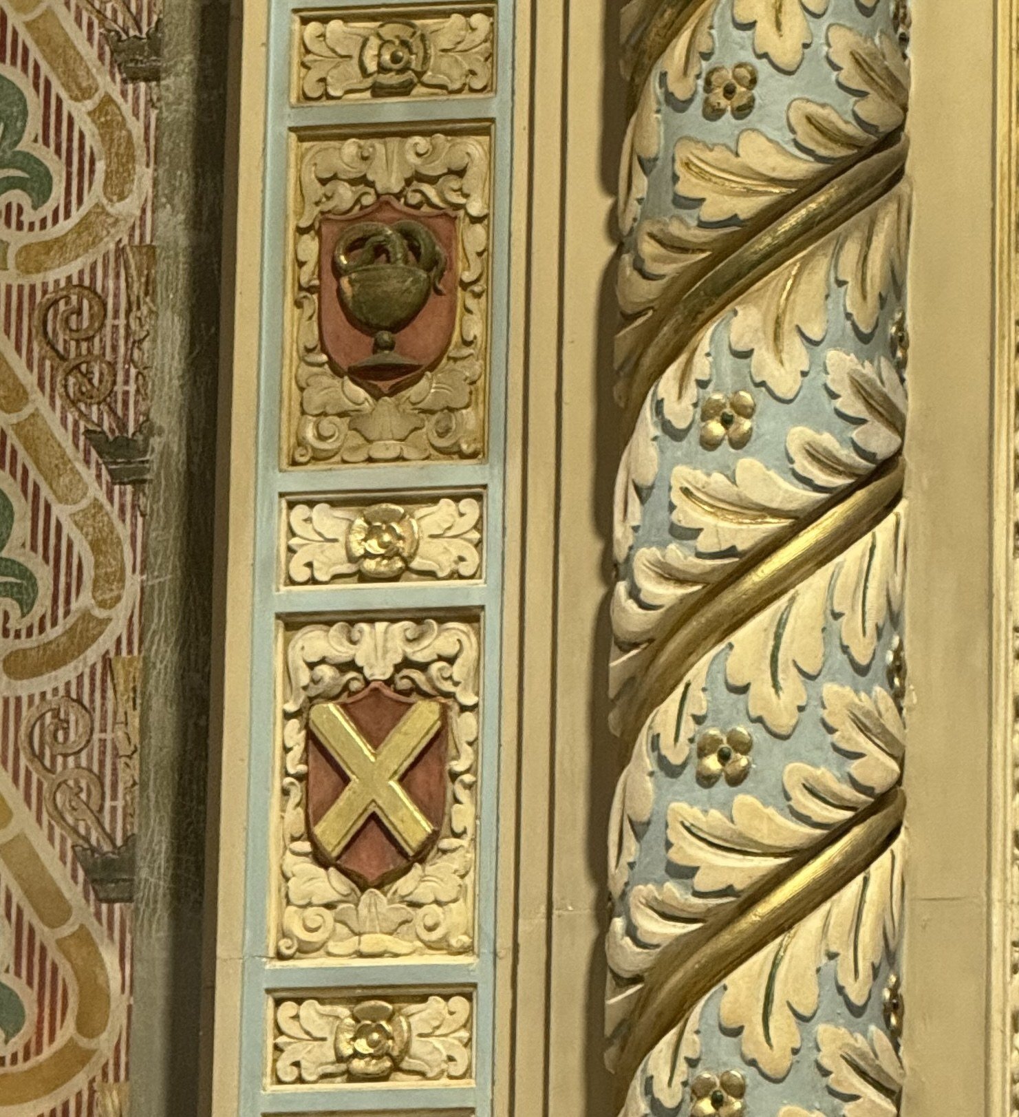 Duller upper chalice ornament and bright gilded lower cross ornament beside a twisted column.