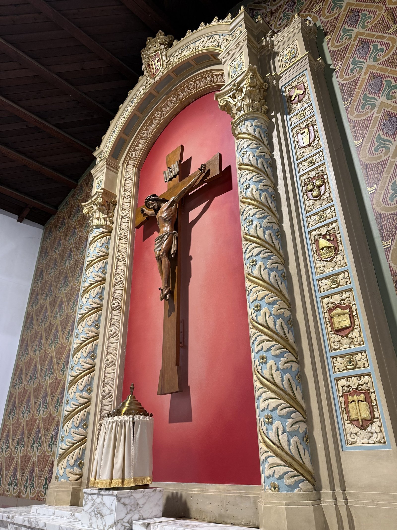 Angled close view of the crucifix, red niche and gilded reredos columns.