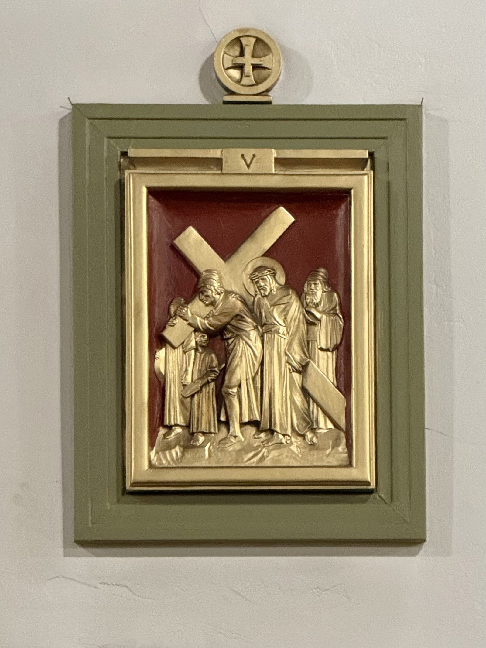 Gold-colored Station V relief against a red background within a green frame.
