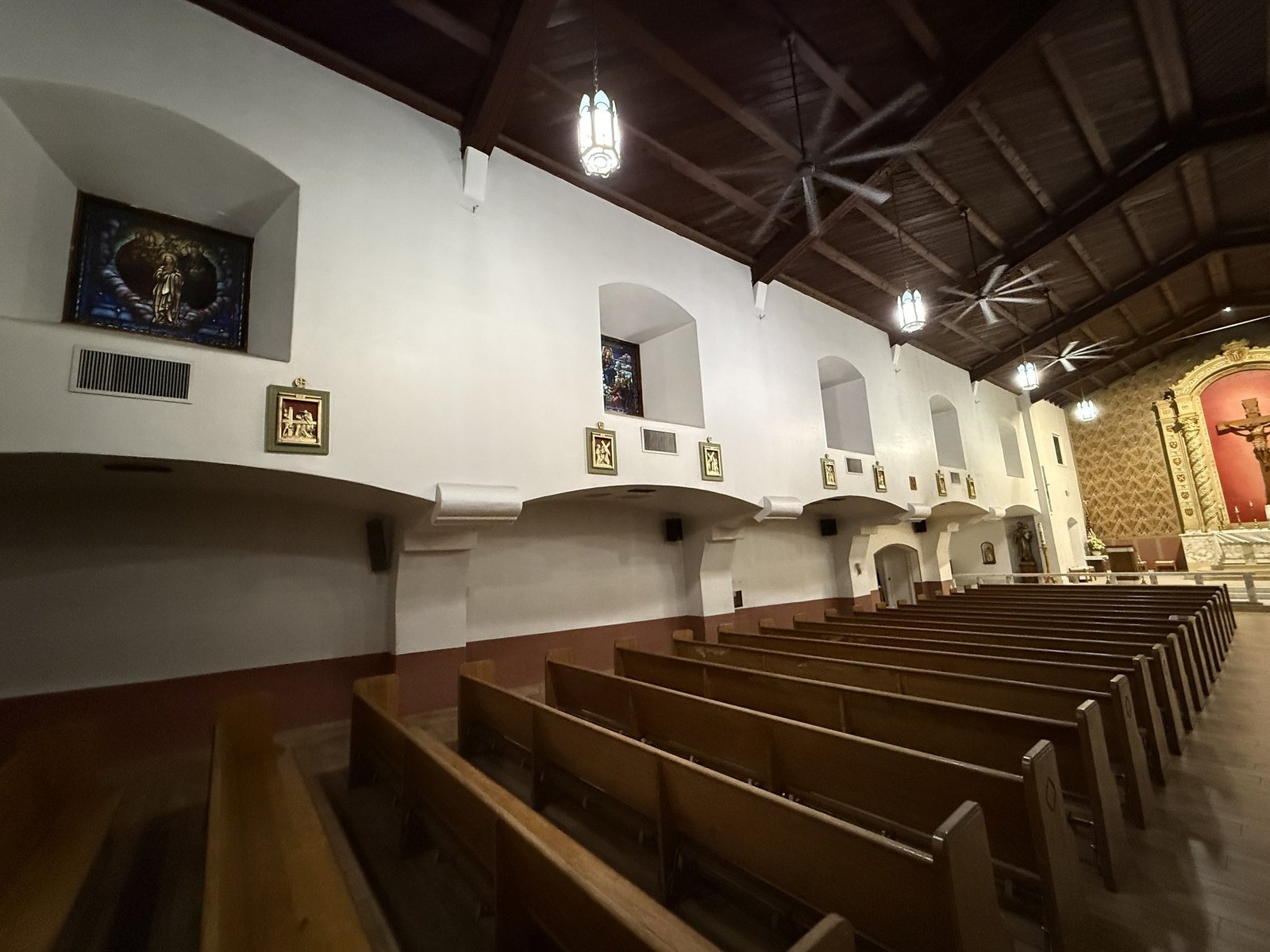 Row of restored Stations along the nave wall above wooden pews.