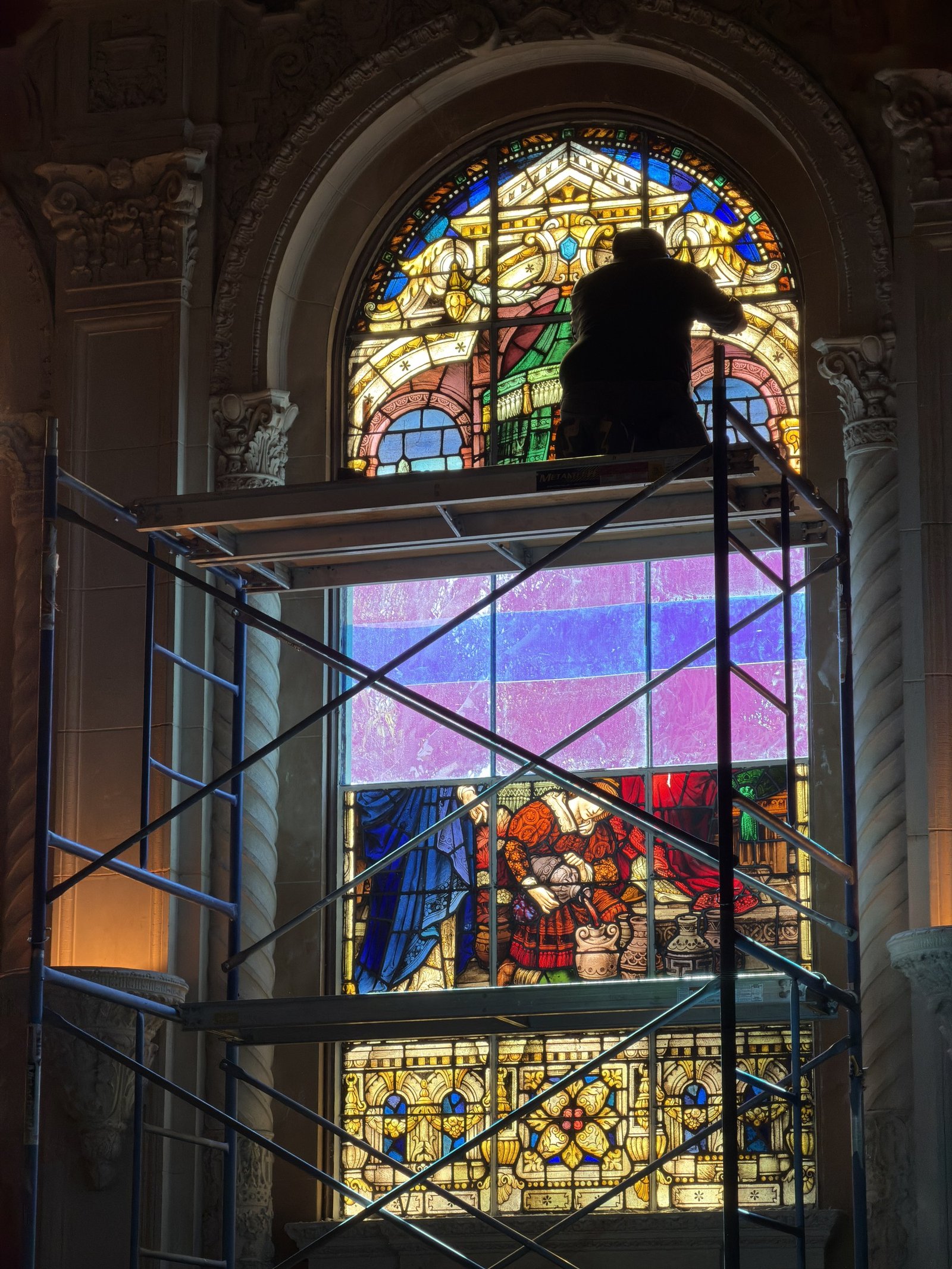 Worker on interior scaffolding at the upper section of an arched stained glass window