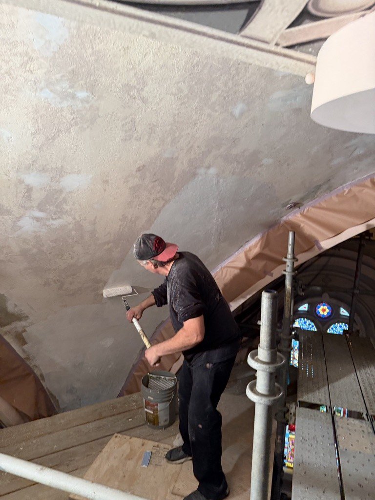 Worker using a roller on the exposed triangular surface above a scaffold platform.