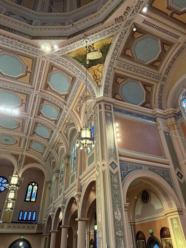 Reinstalled mural high above a decorated column, hanging lantern and church arches.