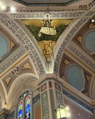 Reinstalled triangular mural with a winged figure, a scroll and a hanging lantern in the foreground.