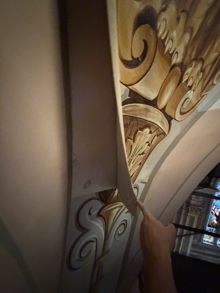 Hand holding the edge of a curved canvas mural beside its decorated architectural border.