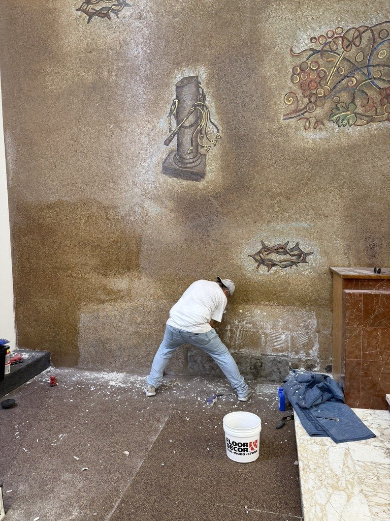 Worker removing material from the lower mosaic wall beside exposed mortar residue.