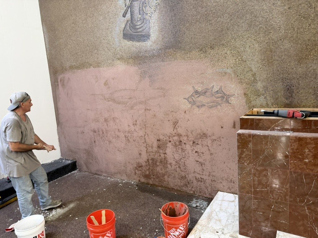 Exposed lower wall area with a crown-of-thorns motif, a worker and tools nearby.
