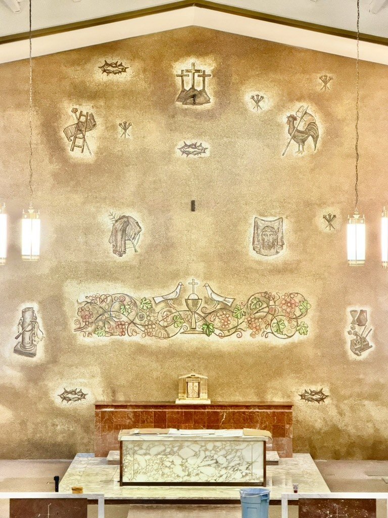 Restored mosaic wall with religious symbols and a grape-and-chalice band above the altar.
